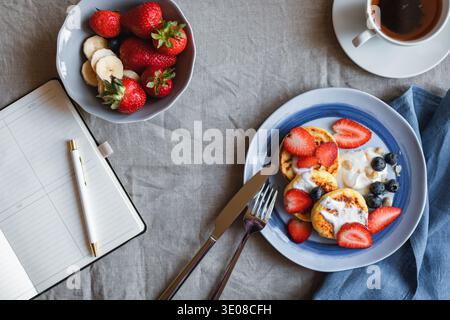 Blick von oben auf hausgemachte Keto Cottage Käse Pfannkuchen mit frischen Erdbeeren und Heidelbeeren, eine Schüssel Erdbeeren und eine Tasse Tee auf einem Tisch Stockfoto