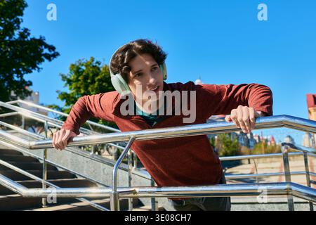Ein junger Mann mit lockigen Haaren entspannt sich draußen in einer Jacke und genießt die Frühlingssonne. Stockfoto