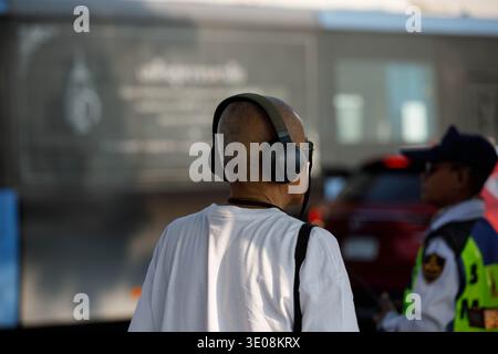 Seniorenmann mit Kopfhörern an der Bushaltestelle, Alltag in der belebten Stadtstraße, Rückansicht, Maharat Road. Stockfoto