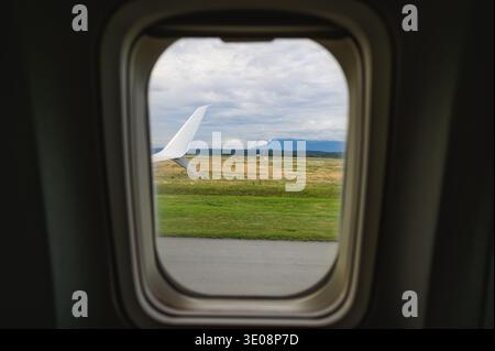 Blick vom Flugzeugflügel, der auf der Start- und Landebahn abhebt, zwischen Feld und bewölktem Flughafen Stockfoto