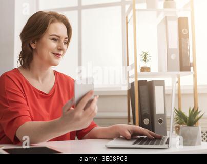 Geschäftsfrau, die auf einem Laptop schreibt und im Büro ein Smartphone verwendet Stockfoto