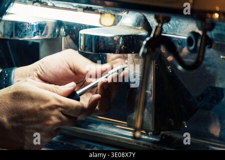 Techniker mit einem Schraubendreher, um die Mutter von der Kaffeemaschine an der Theke im Café zu entfernen. Prozessservice der Gerätewartung in Bever Stockfoto