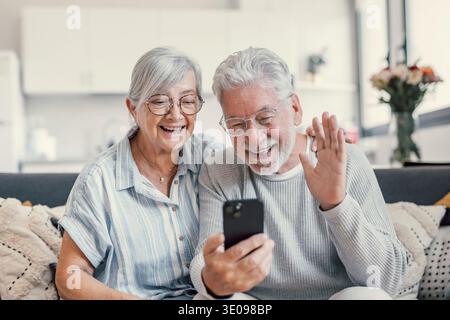 Glückliches Familienpaar im Ruhestand, das für Videoanrufe, Gespräche mit Verwandten, gute Nachrichten, Spaß, Lächeln und Lachen ein Mobiltelefon benutzt. Auto Stockfoto