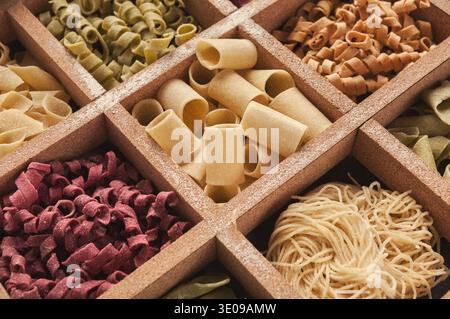 Verschiedene Arten von Pasta, die in einer Sammlung in einer Holzkiste angeordnet sind, unterteilt in Abschnitte Stockfoto