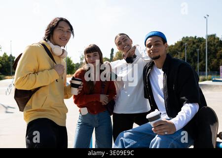 Junge Freunde treffen sich in einem Skatepark und teilen sich Lächeln und Drinks unter einem strahlend blauen Himmel. Stockfoto