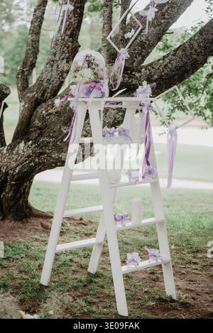 Romantische Hochzeitsdekoration im Freien auf einer weißen Leiter unter einem Baum mit Blumen, Bändern, Kerzen und Geschenkzubehör. Elegantes Cerem Stockfoto