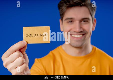 Erfolgreicher Mann In Gelbem Outfit Mit Unbegrenzter Gold-Kreditkarte Auf Blau Stockfoto