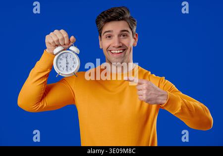 Glücklicher Mann mit Wecker auf Blau. Früher Morgen, richtige Tagesroutine, im Moment leben, jede Minute des Lebens schätzen, Jugend Stockfoto
