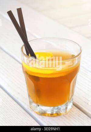 Ein Glas erfrischenden Eistee mit Zitronenscheibe und zwei schwarzen Strohhalmen auf einem weißen Holztisch, perfekt für einen heißen Sommertag Stockfoto