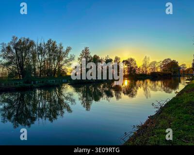 Rijkevorsel, Antwerpse Kempen, Belgien, Sonnenaufgang über ruhigen Kanalspiegeln; goldene Lichtsilhouetten Bäume, glasklare Wasserspiegel, weiche Wolken, kühle Morgenbrise, Ruhe Stockfoto