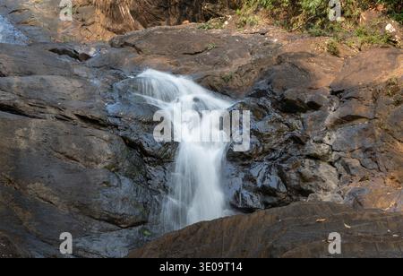 Eine wunderschöne, kleine Kaskade des Ella-Wasserfalls fließt über dunkle, zerklüftete Felsen, umgeben von üppiger grüner Vegetation in Sri Lanka Stockfoto