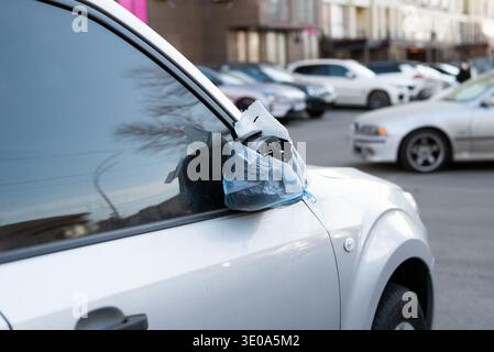 Beschädigter Seitenspiegel in einer blauen Plastiktüte auf einem silbernen Fahrzeug, das in einer Stadtstraße geparkt ist. Stockfoto