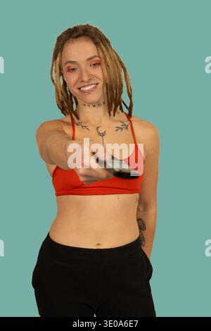 Eine junge Frau mit Dreadlocks und Tattoos, die eine Fernbedienung hält und die Freizeit genießt Stockfoto