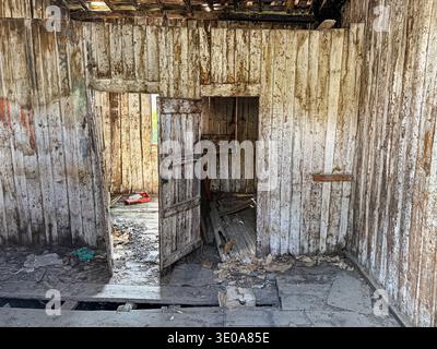 Zwei Türen sind offen in einem leeren Raum eines verlassenen Gebäudes, sodass etwas Licht auf den Schmutz scheint und darin herumschleift. Stockfoto