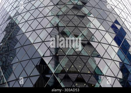 Das markante dreieckige Glasgitter der Hochhausfassade von Gherkin spiegelt die Skyline der Stadt London, England, Vereinigtes Königreich wider. Stockfoto