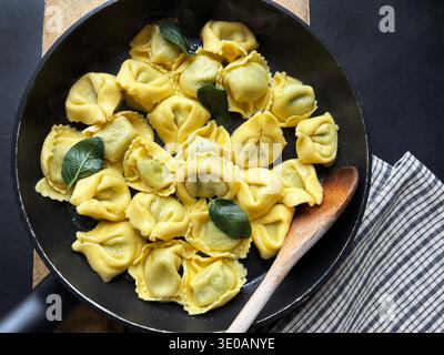 Tortellini gefüllt mit Ricotta und Spinat, in der Pfanne gebraten mit Salbeiblättern auf dunklem Hintergrund. Italienisches Essen. Draufsicht. Stockfoto