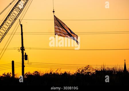 Amerikanische Flagge bei Sonnenuntergang, hängt an einem Kran auf einer Baustelle in Seabright, New Jersey, USA. Stockfoto