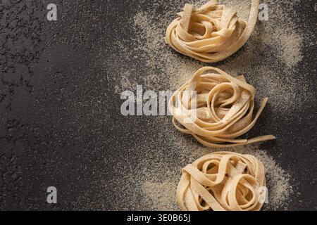 Sammlung von Pasta-Nestern, die auf einer schwarzen Oberfläche angeordnet sind, mit Mehl verstreut Stockfoto