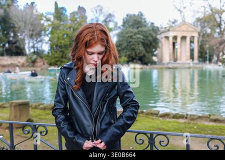 Junge rothaarige Frau in der Nähe des Sees mit historischem Tempel im Stadtpark. Reise-Lifestyle-Szene in einem berühmten europäischen Reiseziel. Stockfoto