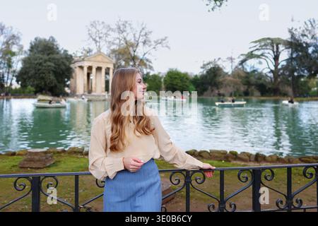 Junge Frau, die den Blick auf den See und den klassischen Tempel im europäischen Park genießt. Reise-Lifestyle-Szene am berühmten historischen Wahrzeichen. Stockfoto