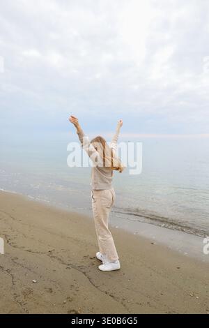 Frau genießt ruhige Küste mit bewölktem Himmel und sanften Wellen. Minimale Küstenlandschaft und Entspannungskonzept. Stockfoto