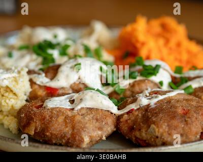 Goldene gebratene Patties glänzen mit cremiger Sauce. Frischer Schnittlauch wird auf dem Gericht mit leuchtendem Grün gestreut. Orangefarbene Karotten verleihen der Mahlzeit eine helle Farbe Stockfoto