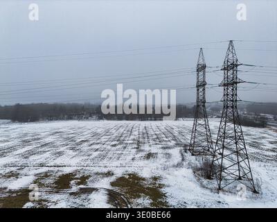 Drohnenansicht von Hochspannungsleitungen in verschneiten Winterlandschaften Stockfoto