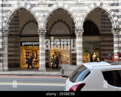 Goldenpoint-Geschäft unter gestreiftem mittelalterlichem Portikus an der Via XX Settembre, Genua, Italien. Die Käufer laufen vorbei an luxuriösen Schaufenstern im Einzelhandel. Stockfoto