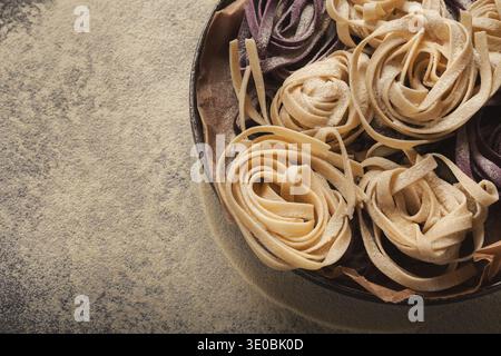 Sammlung farbenfroher Pasta, die ordentlich in einer Schüssel auf einer strukturierten Oberfläche angeordnet sind Stockfoto