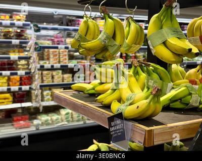 Bananen, die in einem Marks & Spencer Food Hall Supermarkt zum Verkauf angeboten werden, wobei die Gänge im Hintergrund sichtbar sind. Stockfoto