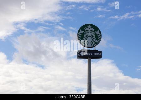 Das legendäre Starbucks Coffee Round Green Logo und das Drive Thru Richtungsschild auf einer hohen Stange vor einem blauen Himmel mit weißen Wolken in der Stadt Stockfoto
