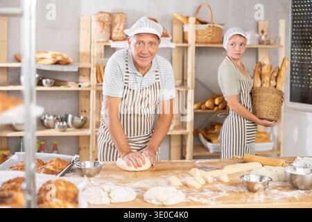 Senior Mann arbeitet in der Bäckerei als Bäcker, Knete Teig, arbeitet mit Mehl. Stockfoto