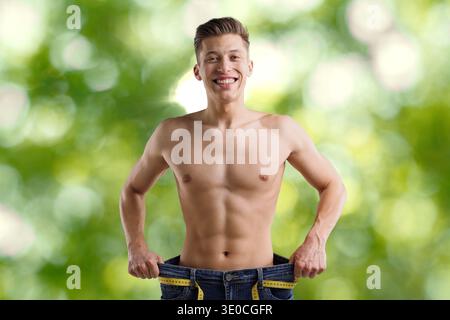 Glücklicher Mann in seiner alten Jeans vor verschwommenem grünem Hintergrund. Gewichtsverlust Stockfoto
