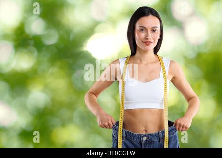 Glückliche Frau in ihrer alten Jeans vor verschwommenem grünem Hintergrund. Gewichtsverlust Stockfoto