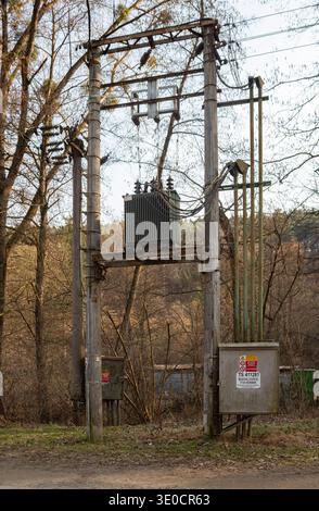 Ein veralteter elektrischer Transformator und Stromleitungen am Rande eines Waldes Stockfoto