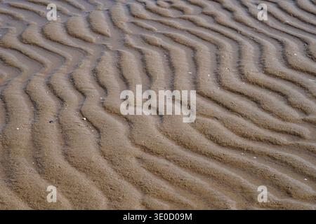 Nach der Ebbe werden Schichten von Wellenstrukturen am Strand hinterlassen, und die nasse Sandoberfläche ist unter der Lichtbrechung zart und glänzend, showi Stockfoto