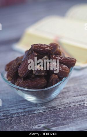 Eine Schüssel Datteln auf einem Holztisch mit einem Buch im Hintergrund Stockfoto