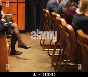 Eine offene Nahaufnahme fängt eine Frau ein, die in einem Publikum sitzt und sich auf ihr Smartphone konzentriert. Die nachdenkliche Atmosphäre bei schlechten Lichtverhältnissen unterstreicht Stockfoto