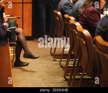 Eine offene Nahaufnahme fängt eine Frau ein, die in einem Publikum sitzt und sich auf ihr Smartphone konzentriert. Die nachdenkliche Atmosphäre bei schlechten Lichtverhältnissen unterstreicht Stockfoto