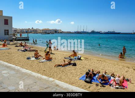 01.09.2025, Griechenland, Mykonos, Mykonos - Touristen und Einheimische genießen das Schwimmen am kleinen Stadtstrand von Paralia Choras Mikonou, direkt neben dem alten Haus Stockfoto