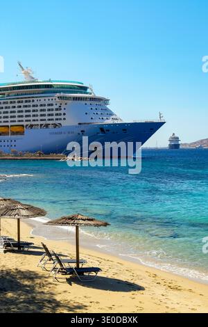 02.09.2025, Griechenland, Mykonos, Mykonos - das Kreuzfahrtschiff Voyager of the Seas liegt im Hafen von Mykonos. Im Vordergrund stehen Liegestühle und Sonnenschirme auf dem t Stockfoto