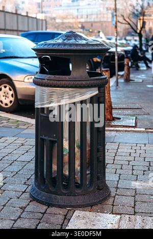 Mülltonne steht an einem bewölkten Tag in einer Stadt in der Nähe geparkter Autos auf der Straße Stockfoto
