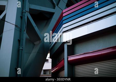 Abstrakte architektonische Details am Tsutenkaku Tower Base, Shinsekai, Osaka, Japan. Stahlversteifung, magentafarbene und blaue Fassade. Stockfoto