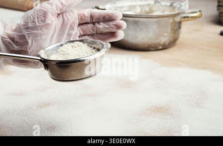 Männliche Hände sieben Mehl aus dem Sieb auf hölzernem Küchentisch Stockfoto