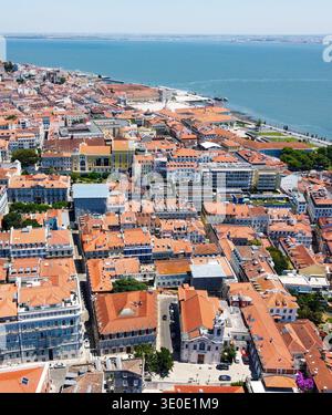 Aus der Vogelperspektive auf Terrakotta-Dächer, die unter einem weiten, offenen Himmel in Richtung Tejo kaskadieren, Lissabon, Portugal. Stockfoto