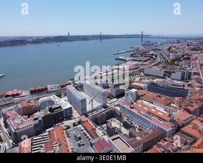 Aus der Vogelperspektive treffen die Terrakotta-Dächer auf den Fluss Tejo, im Schatten der Ponte 25 de Abril, Lissabon, Portugal. Stockfoto