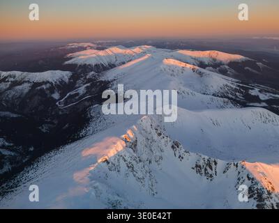Aus der Vogelperspektive auf schneebedeckte Gipfel, geküsst vom warmen Schein der untergehenden Sonne, die einen atemberaubenden Kontrast zu den kalten, schattigen Tälern Nizke Tat bilden Stockfoto