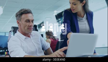Zeigende Frau in blauem Blazer, die sich im Büro über den Laptop stützt, Kollege arbeitet mit Avatar-Grafiken Stockfoto