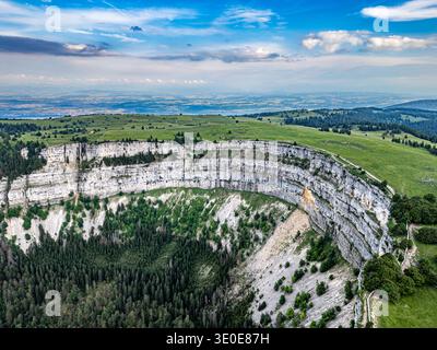 Blick aus der Vogelperspektive auf die atemberaubende, geschwungene Creux du Van, wo weiße Klippen auf einen dunklen Waldboden unter einem riesigen Himmel treffen, Creux du Van, Neuchâtel, SW Stockfoto