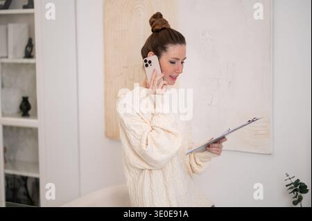 Frau in weißem Pullover, die am Telefon spricht und zufrieden aussieht Stockfoto
